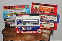 Seven vintage diecast toy trucks in original packaging displayed on a wooden surface. Boxes show various trucking companies and brands with colorful graphics.