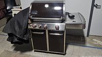 Front angle view of Weber Genesis gas grill with closed hood and cover draped over one side