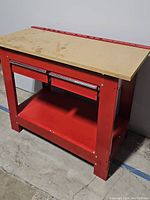 Front and side view of the red metal work bench with wooden top, drawers, and open shelf underneath.