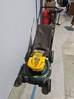 Front view of Yard Man push lawn mower showing yellow engine cover, green mower deck, black grass catcher back, and black wheels.