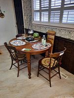Four antique wooden chairs around a dining table, seats with drilled hole ply wood design and brown cushion pads