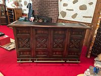 Front view of bar cabinet with drop leaves folded up, showing raised panel front doors, molded top edge and brass-tone foot rail on castors