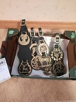 Four brass buckles attached to black leather straps displayed in a box