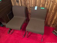 Four stackable chairs with steel frames and brown upholstery shown on red carpet against wood paneled wall.