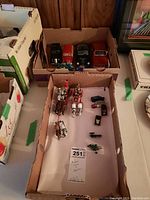 Overview photo showing collectible miniature cars and detailed horse-drawn carriages arranged in cardboard boxes.