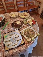 Overview of 11 decorative and collector plates displayed on table with vintage wooden chairs in background.