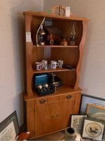 Full image of the wood corner cabinet showing shelves with various items, one drawer, and lower cabinet doors. Cabinet dimensions are approximately 43x20x73 inches.