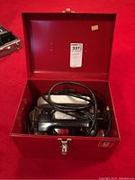 Red metal storage case with the circular saw inside, showing wires and power cord coiled.