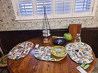 Photo of the complete set on a wooden table including fondue pot on stand, fuel canister, forks, glass bottle, sectional plates stacked, and fabric placemats.