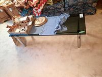 Rectangular coffee table with dark tinted glass top and metal tubular legs taken from an angle showing side and top view with blue cloth and wooden objects on top