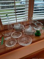 Wide view of all glassware including decanter, vases, plates, and bowls on window sill