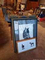 The framed black and white horse head print in gray and black frame along with the smaller rectangular wooden frame showing two horse tiles, placed on a carpeted floor with room furniture background.