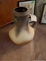 Front side of a large ceramic jug showing the gradient cream to brown glaze and textured rim with handle