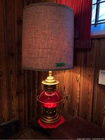 Photo showing lamp with lit base glowing red, beige fabric cylindrical shade, and wooden background