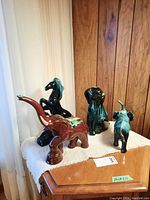Photo showing all four pottery animal figurines arranged on a cloth atop a wooden surface, background wood panel wall.