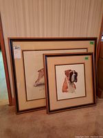 Two framed Robert J. Mary prints of boxer dogs, one smaller and one larger, both leaning against a wooden wall.