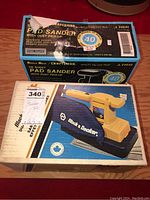 Two boxed sanders, Craftsman in original box and Black & Decker in yellow with dust bag attachment visible