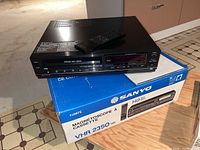 Front and top view of Sanyo VHR 2350 VHS player placed on original branded box with remote on top.