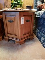 Side view of hexagonal wooden side table cabinet with door and metal handle, placed between sofa and wall.