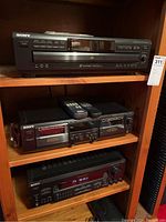 Front view of all three Sony stereo components stacked on a wood shelf: CD player on top, cassette deck with two remotes in middle, receiver on bottom.
