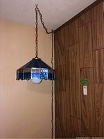 Stained glass lamp hanging from ceiling with chain, showing overall view including bulb and chain length.
