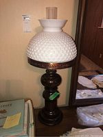 Table lamp unlit showing the dark wood base, hobnail patterned white glass shade, pierced metal detail ring, and clear glass chimney.
