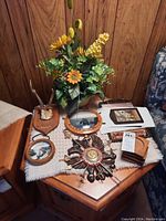 Lot of wall hanging decorations including faux floral arrangement, wooden plaques, coasters, and a sunburst-style decorative piece on a wooden table.