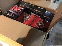 Open cardboard shipping box showing 20 sealed Ottawa Senators bobblehead boxes arranged inside. Various players visible on packaging with team colors and logos.