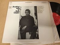 Back cover of Bob Dylan LP 'Another Side of Bob Dylan' showing black-and-white photo of Bob Dylan, track listing, and partially visible vinyl record with red label.