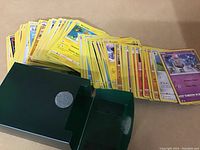 Green box containing 100 Pokémon cards with various energy and Pokémon types visible, cards have yellow borders.