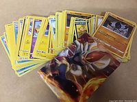 50 Pokémon trading cards spread out partially with a visible sleeve or binder showing a fire-type Pokémon on the cover.