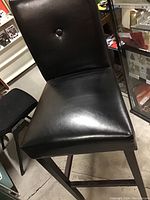 Full view of black bar chair showing padded seat and back with single button tuft on backrest, dark wood legs.