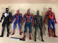 Photo of five large Spider-Man action figures in various suits and colors laid flat on a surface