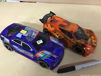 Pair of translucent large friction cars, blue and orange, with a Sharpie marker for size scale.