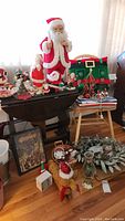 Full lot overview showing multiple Santa decorations, linens, candleholders, and other items stacked on tables and floor