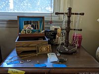 Open wooden jewelry box on desk with broken mirror inside lid, assorted rings and necklaces visible, sonic cleaner box behind, wooden necklace stand loaded with chains