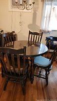 Round pine dining table with four matching chairs in a room corner, showing full arrangement and dark wood finish.