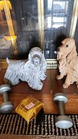 Two plaster dog figurines and front view of weights on wooden surface with glass and brass fireplace screen behind