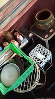 Various items including pottery planters, metal plant stands, small table, roller skates, and magazine rack arranged together in sun room area. Green crate contains miscellaneous items.