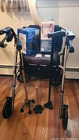 Photo of Hugo rollator walker with handbrake and seat, two canes and Walgreens blood pressure monitor box placed on walker seat, taken from front.