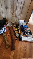 Photo showing various household and cleaning items including a brown draft stopper, a cooler bag, toilet wax ring, WD-40, duct tape, and other miscellaneous items on the floor against a wooden wall.