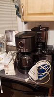 Photo showing multiple coffee makers, a food chopper, and a blender on a kitchen counter under cabinets.