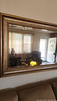 Full view of the mirror on the wall above a couch showing the wooden frame with gold and brown two-tone finish reflecting the living room.
