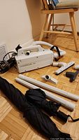 Overall view of vacuum cleaner, hose, attachments, and umbrellas laid on wooden floor.