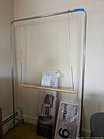 Full view of a metal garment rack with adjustable two-tier bars and caster wheels. Includes packaging for components and hangers visible in front of the rack.