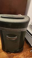 Full view of the black OfficeMax OMO2750 shredder with mesh bin and handle, showing condition and size.