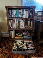 Full view of wooden bookcase filled with VHS tapes and books, showing overall condition and content