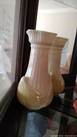Photo of a cream and yellow decorative vase with vertical ridges and beaded rim detail, shown against a mirror reflecting the item.