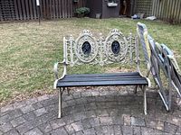 Full view of the outdoor metal framed bench with wood seat and detailed metal back, placed on outdoor pavers with grass in the background.