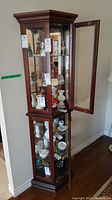 Curio cabinet standing upright with glass shelves visible through side and front glass panel doors which are open.